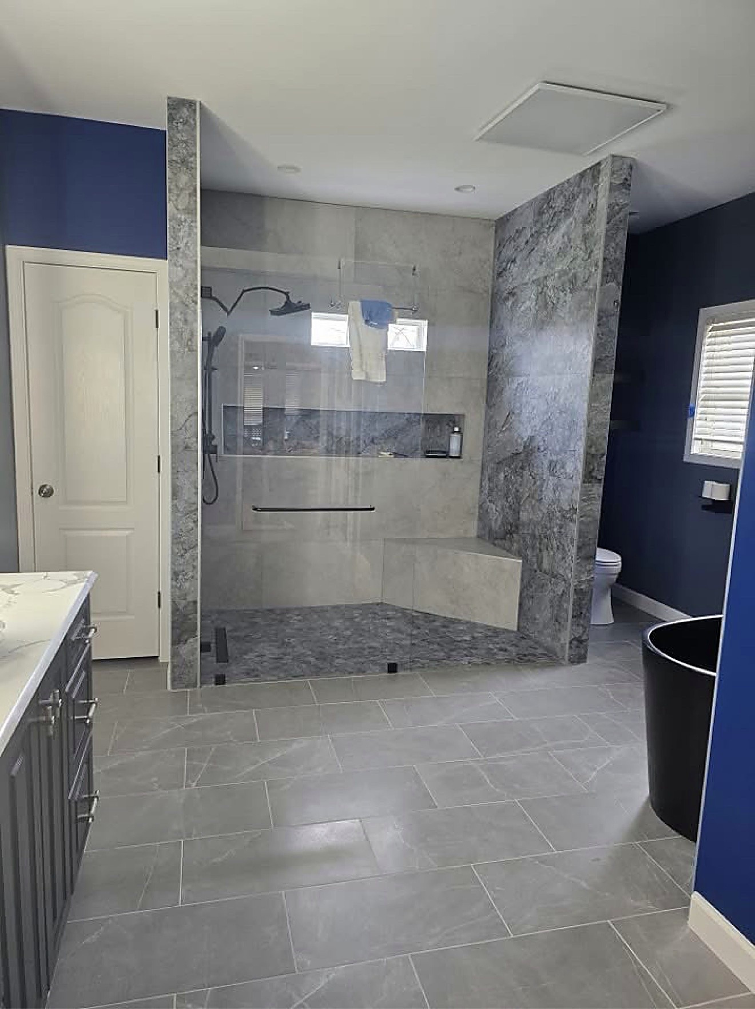 Remodeled bathroom with a glass shower, marble tile and fresh navy walls